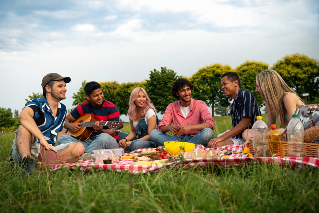 Group of multiethnic teenagers spending time outdoor on a picnic at the park. Concept about generation z, lifestyle and friendship
