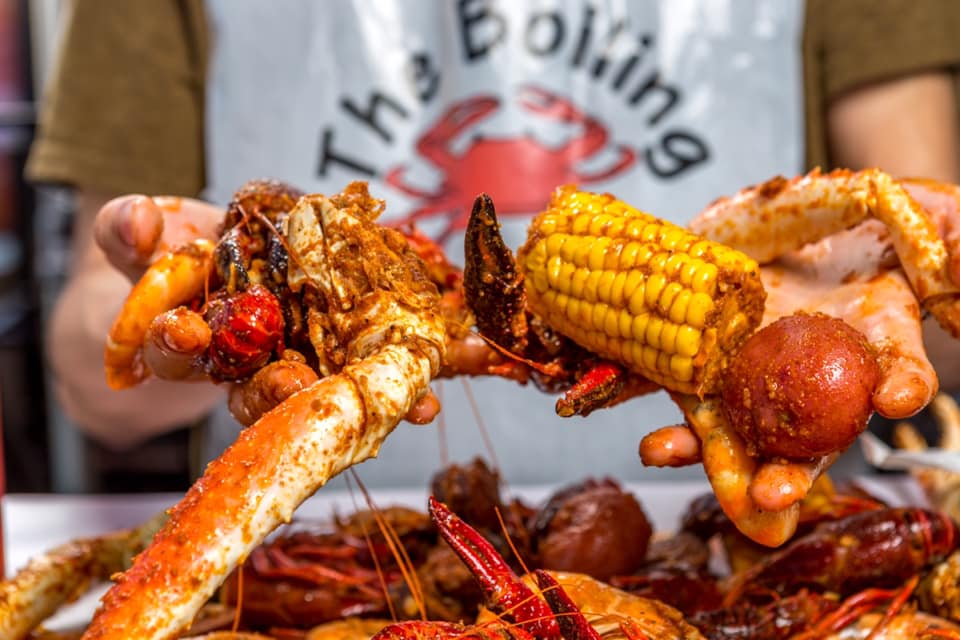 Closeup of hands holding grab legs and corn on the cob at The Boiling Crab in Torrance