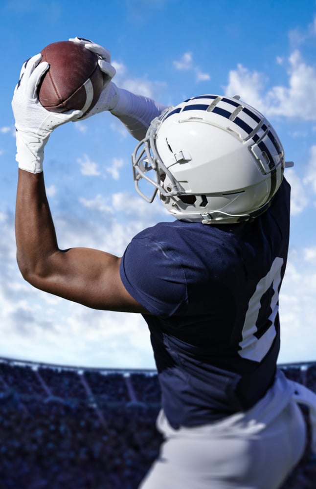 Football player jumping up mid-catch during a game in a stadium