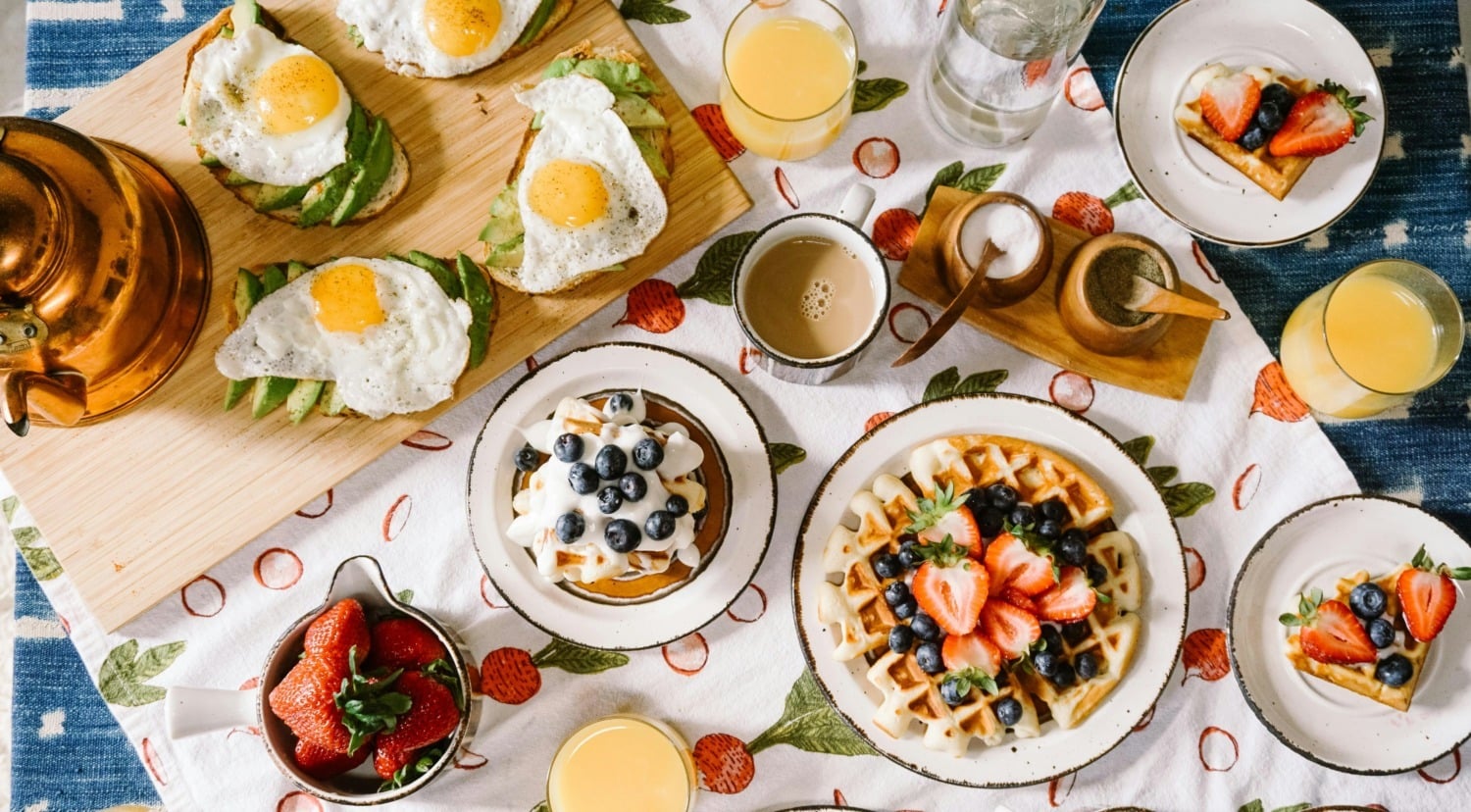 Brunch plates on a table including waffles, avocado toast, coffee and more