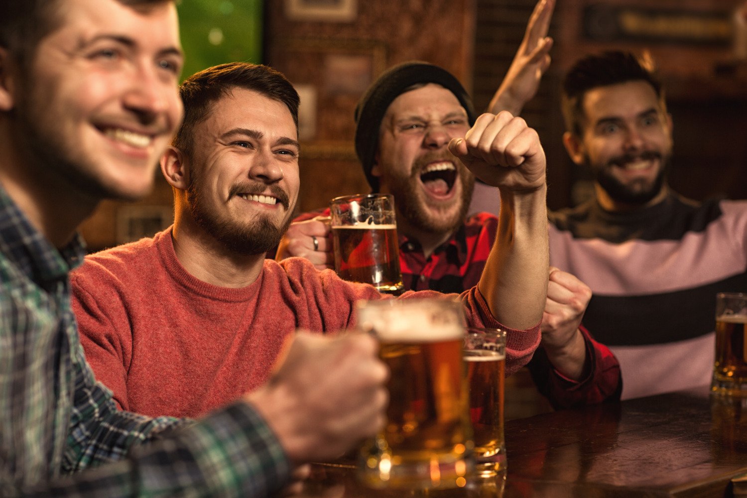 Group of friends holding beer and cheering on their favorite team at a watch party