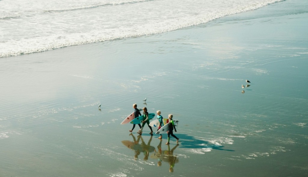 Kids walking along the beach shore with surfboards