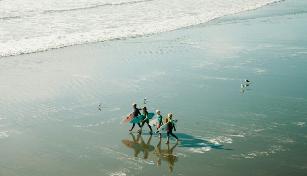 Kids walking along the beach shore with surfboards